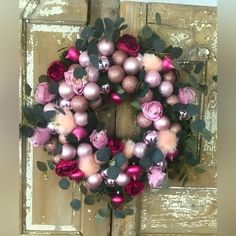 a wreath with pink and red ornaments hanging on a door