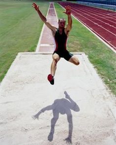 a man is jumping in the air on a track with his hands up and feet apart