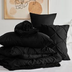 a pile of black pillows sitting on top of a white bed next to a painting