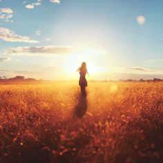 a woman standing in the middle of a field at sunset