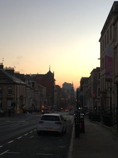 a car parked on the side of a road next to tall buildings at sunset or dawn