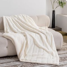 a couch with a blanket on top of it next to a vase filled with flowers