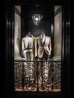 two men's suits are on display in front of a window with iron bars