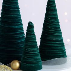 three green christmas trees sitting on top of a white table next to a gold ornament