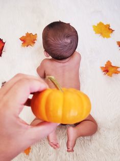 a baby is sitting on the floor with a pumpkin in his hand and leaves around him