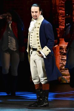 a man in uniform standing on stage with other men behind him and one wearing a coat