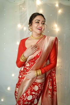 a woman in red and gold sari posing for the camera with her hands on her hips