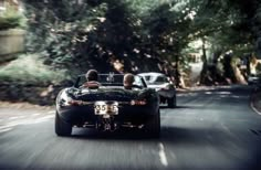 two cars driving down the road with trees on both sides and one car behind them