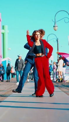 two people are dancing on the sidewalk in front of some buildings and one person is wearing red pants