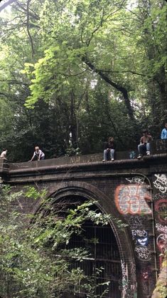 people are sitting on the edge of an old bridge with graffiti all over it and trees in the background