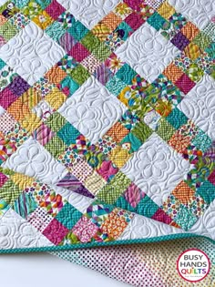 a quilted table topper with colorful squares and flowers on the edges, sitting on a white wooden surface