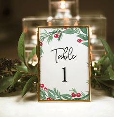 the table numbers are displayed in front of candles and greenery with berries on them