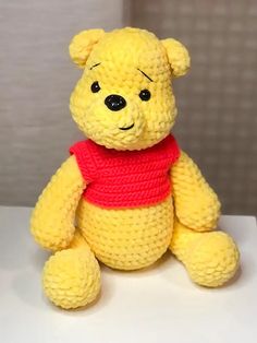 a yellow teddy bear with a red scarf around it's neck sitting on a white surface