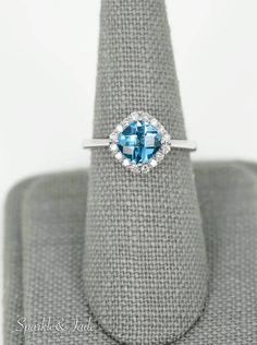 a blue topazte and diamond ring sits on a gray cloth with a white background