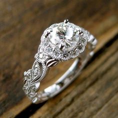 a white gold engagement ring with an intricate design on the band and round brilliant cut diamond center