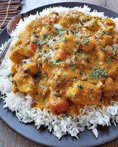 a blue plate topped with rice covered in curry and chicken next to a fork on top of a wooden table