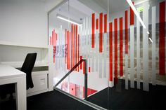 an office with red and white stripes on the glass wall, black chair and desk