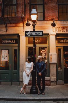 a man and woman standing next to a lamp post in front of a storefront