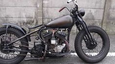 an old motorcycle is parked in front of a concrete wall and has black paint on it