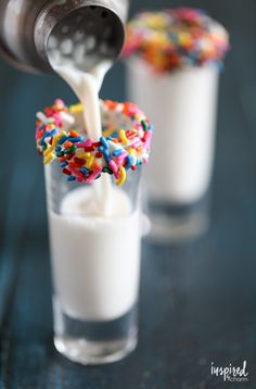 a spoon pouring milk into a glass filled with sprinkles