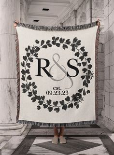 a woman holding up a white and black wedding blanket with the initials r & s on it