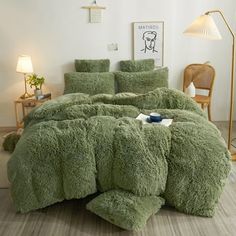 a bed covered in green fluffy comforter and pillows with two lamps on either side