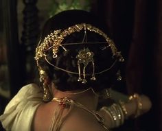 the back of a woman's head with gold jewelry on her neck and shoulders