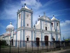 an old white church with blue trim and steeples on the front, surrounded by black iron fence