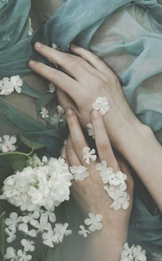 two hands touching each other with white flowers in the foreground and blue silk on the background