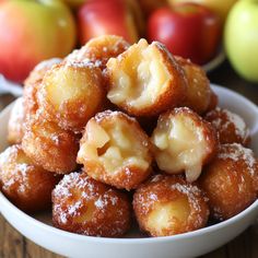 a white bowl filled with donuts covered in powdered sugar next to some apples