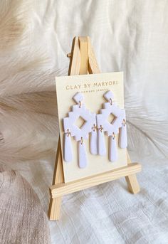 the clay earrings are on display in front of an easel with white furnishing