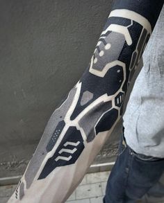 a man with a black and white tattoo on his arm is standing in front of a gray wall