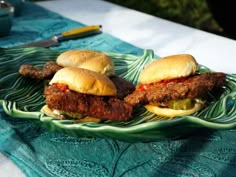 two sandwiches on a green plate sitting on a blue towel next to a knife and fork