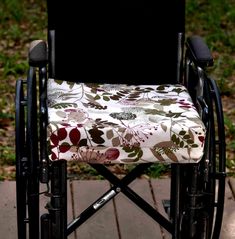 a chair with a flowered seat cover sitting on a brick walkway in front of some grass