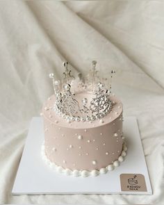 there is a pink cake with pearls and a crown on top that has been frosted