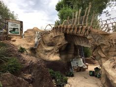 the entrance to an artificial dinosaur park is made out of rocks and wood, with plants growing on top