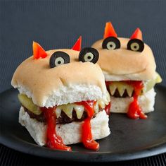 two sandwiches with monster eyes and teeth on them are sitting on a black plate, one is cut in half