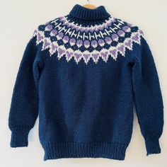 a blue sweater with purple and white designs on the collar is hanging from a wooden hanger