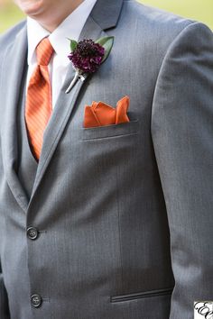 a man in a gray suit with an orange flower on his lapel