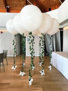 some white balloons and greenery are hanging from the ceiling in an indoor function hall