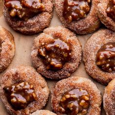 chocolate covered doughnuts are arranged on a brown paper lined baking tray with powdered sugar and caramel drizzle