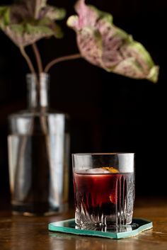 a drink sitting on top of a coaster next to a vase with a plant in it