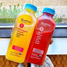 two bottles of juice sitting next to each other on a window sill in front of a person