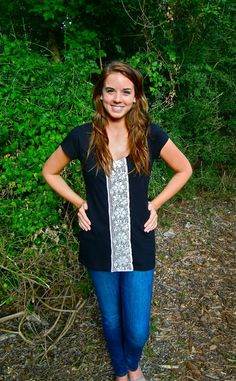 a woman standing in front of some trees and bushes with her hands on her hips