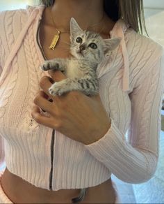 a woman holding a small kitten in her arms while wearing a pink sweater and gold necklace