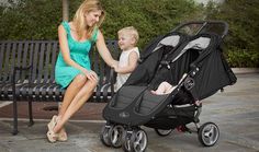 a woman sitting on a bench next to a baby in a stroller and holding the hand of her child