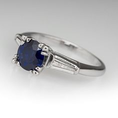 The ring is centered with one (1) round mixed cut natural sapphire set into a four-split prong setting. The shoulders of the ring are each accented with one (1), channel set, tapered baguette cut diamond. The ring measures 6.7mm at the top, rises 7.3mm above the finger, tapering to 1.8mm wide and 1.2mm thick at the base of the shank. The ring is currently a size 5.25. Round Sapphire Ring, Blue Sapphire Engagement Ring, Round Sapphire, Sapphire Engagement Ring Blue, Sapphire Engagement Ring, Baguette Cut Diamond, Channel Set, Baguette Cut, Sapphire Engagement