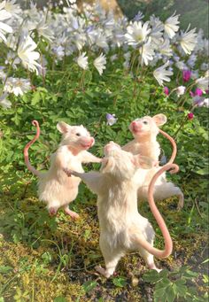 two toy mice playing with each other on the ground in front of flowers and grass