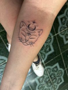 a woman's leg with a cat tattoo on her left arm and the moon behind it