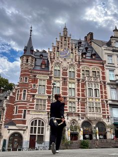 a woman is walking in front of an old building with many windows and clock on it